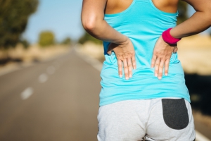 Female runner athlete back injury and pain. Woman suffering from painful lumbago or kidney illness while running in rural road.