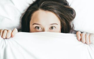 Woman looking out from under her duvet